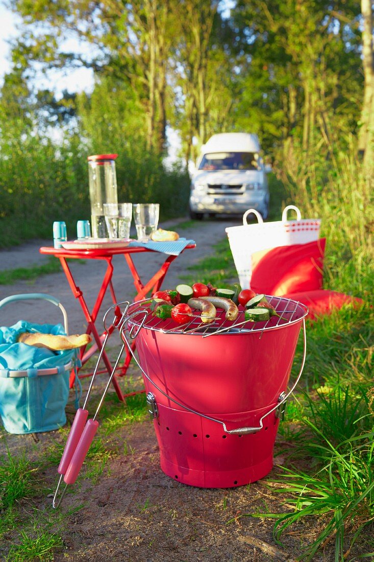 A barbecue, a camping table and a basket on the edge of a road