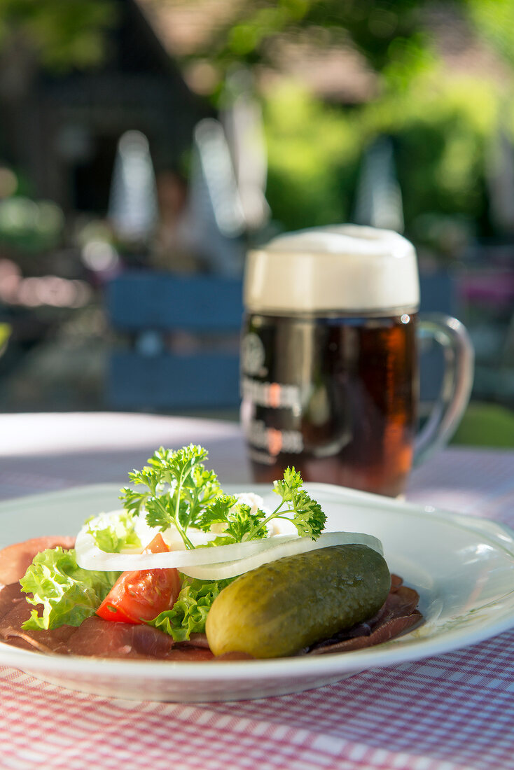 Brotzeit mit Schinken, Essiggurke & Bier auf Tisch im Freien