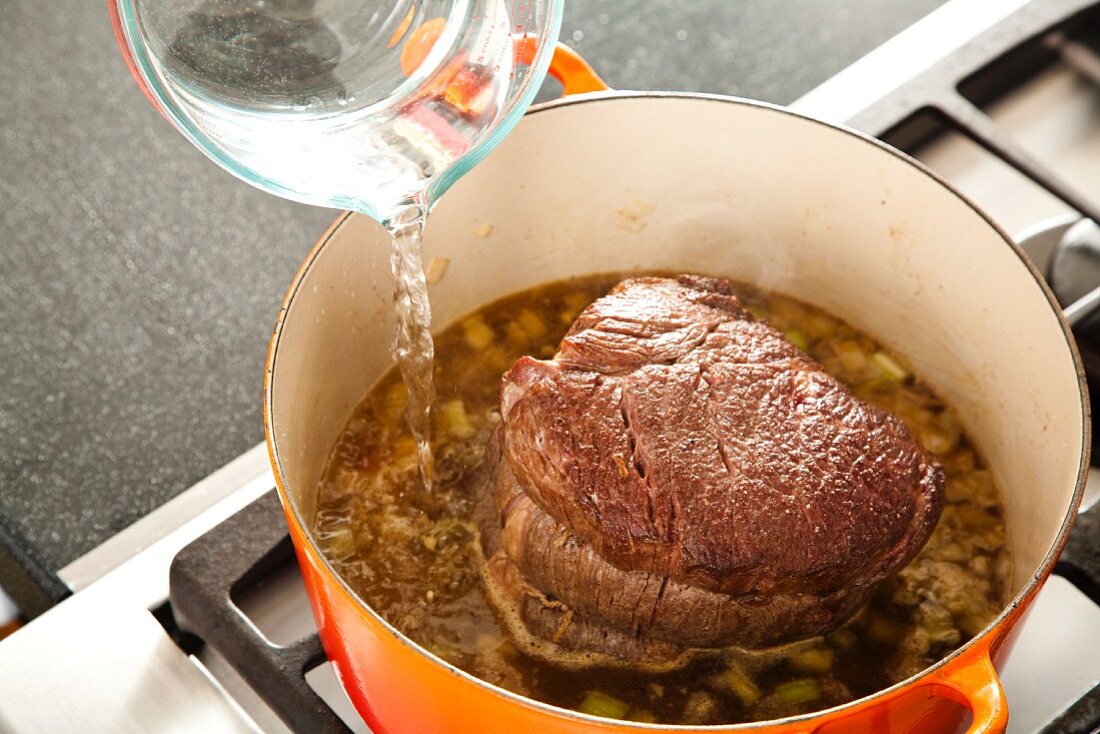 Pouring Water into a Pot of Broth with a Pot Roast