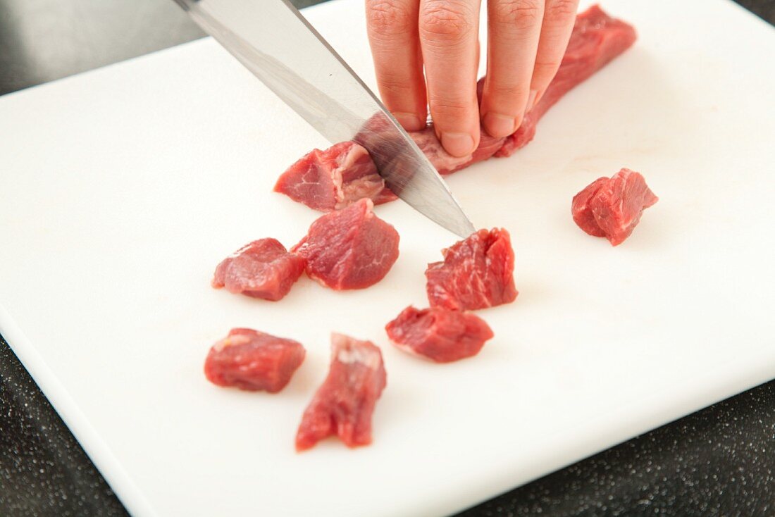 Cutting Lamb into Cubes on a Cutting Board