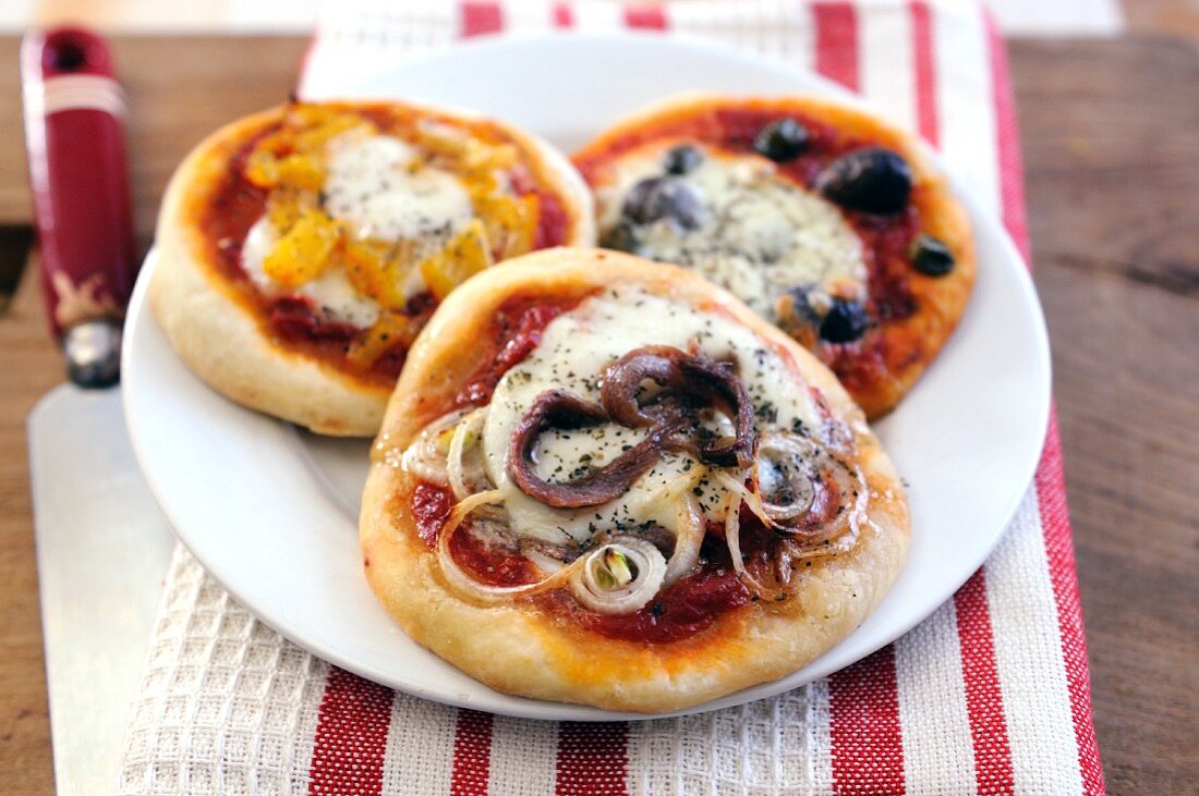 Three mini pizzas with different toppings and mozzarella