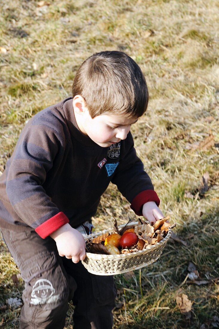 Kleiner Junge trägt Körbchen mit gefärbten Ostereiern