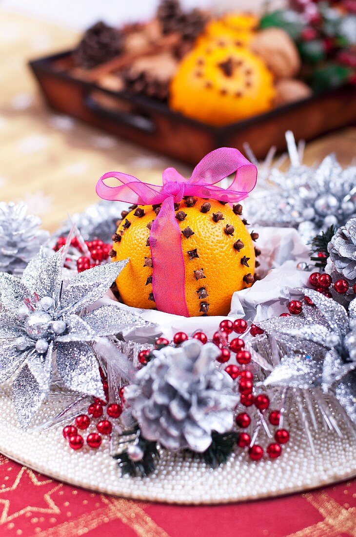 An orange pierced with cloves amongst silver Christmas decorations