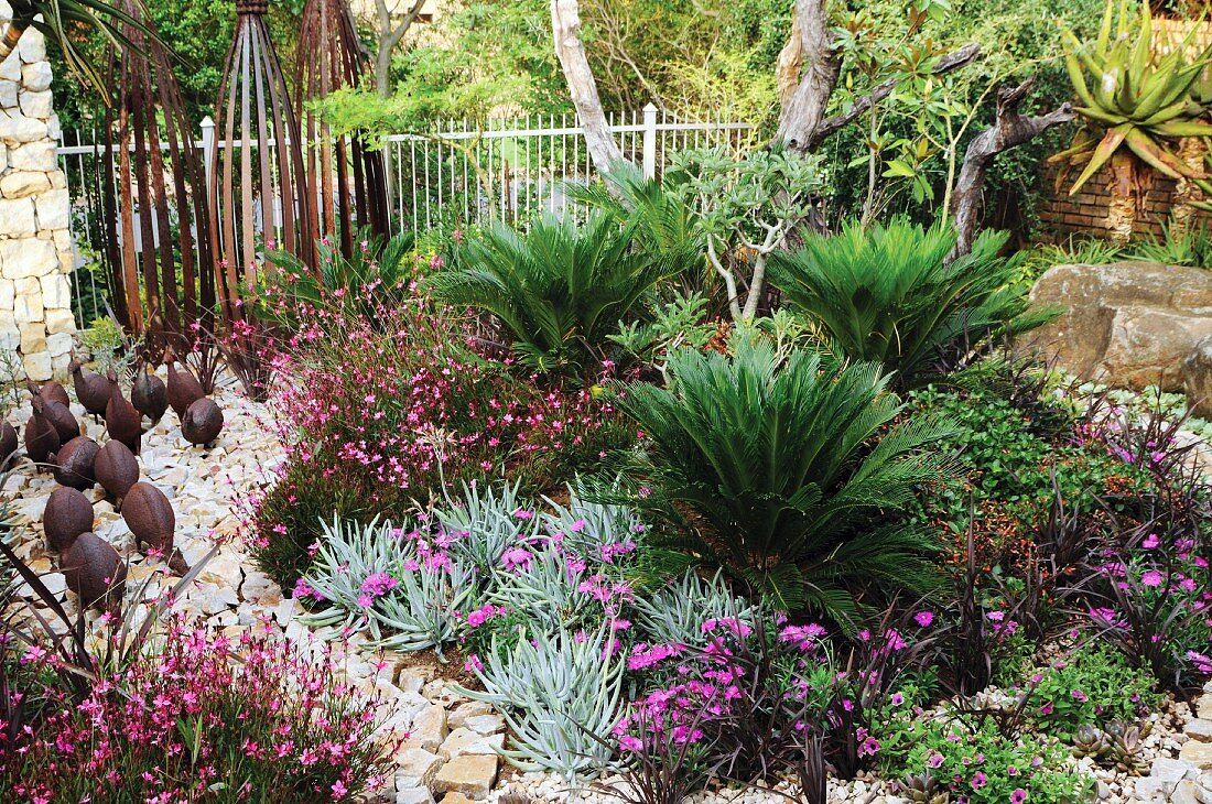 Exotisch gestalteter Gartenbereich mit Palmfarnen, Sandsteinweg & Tierfiguren