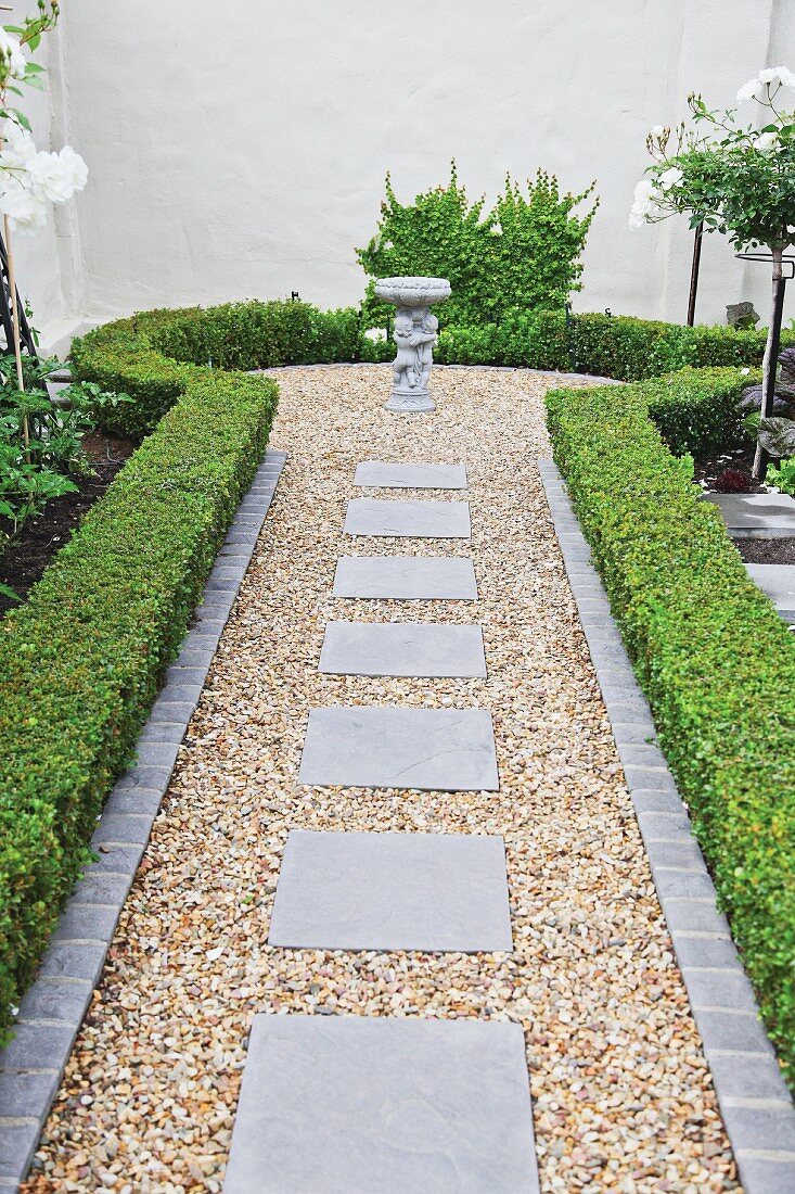 Gravel path with small, circular bay lined with clipped hedges and tall garden wall