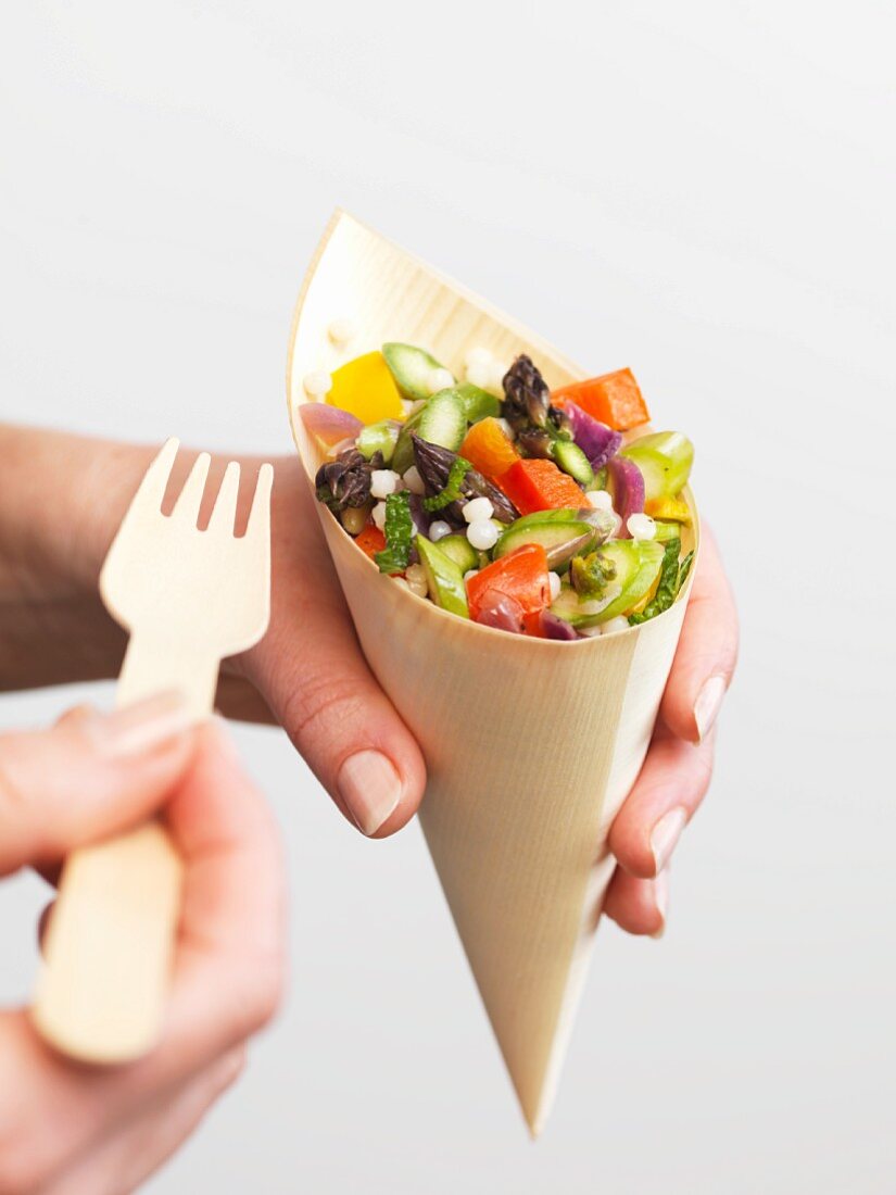 A woman holding a cone of couscous and asparagus salad