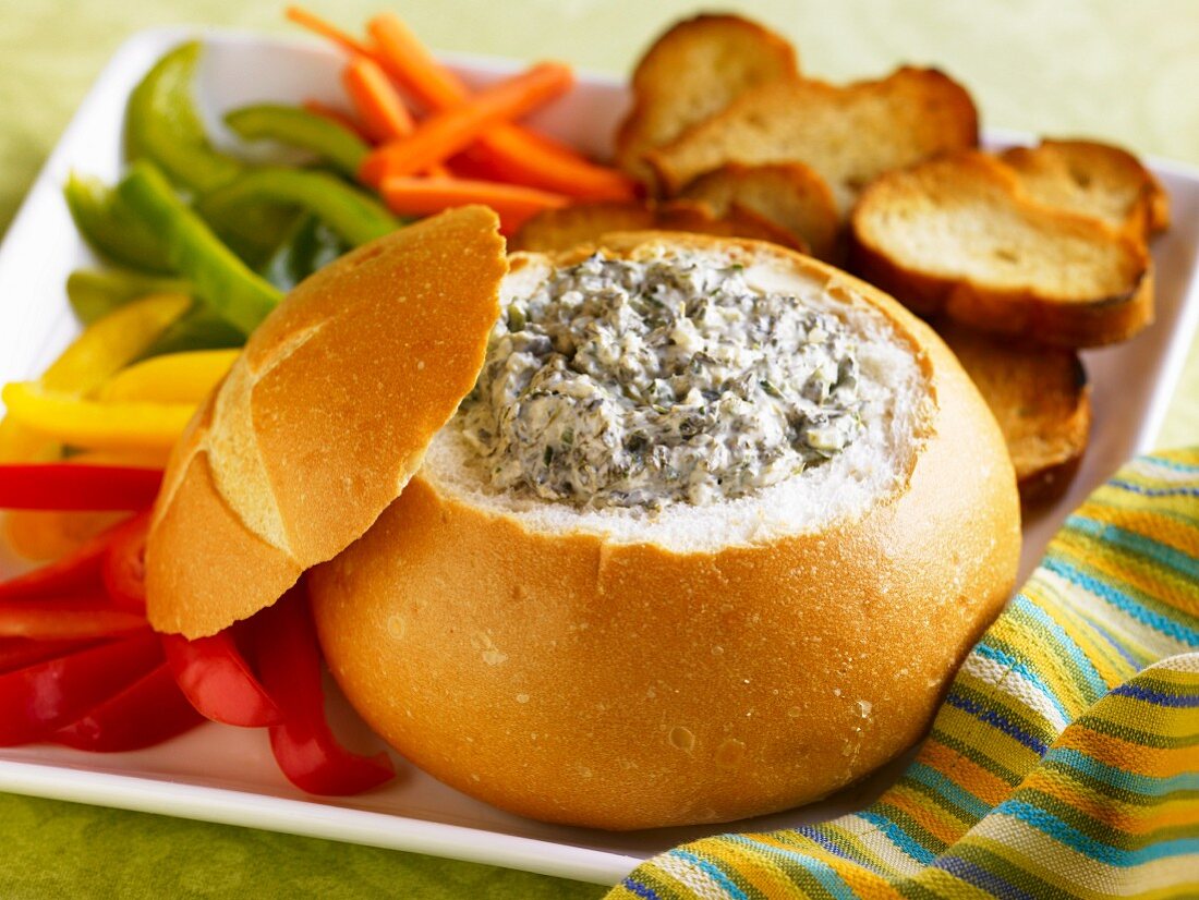 Spinach Dip in a Bread Bowl with Sliced Veggies and Toasted Bread Slices for Dipping