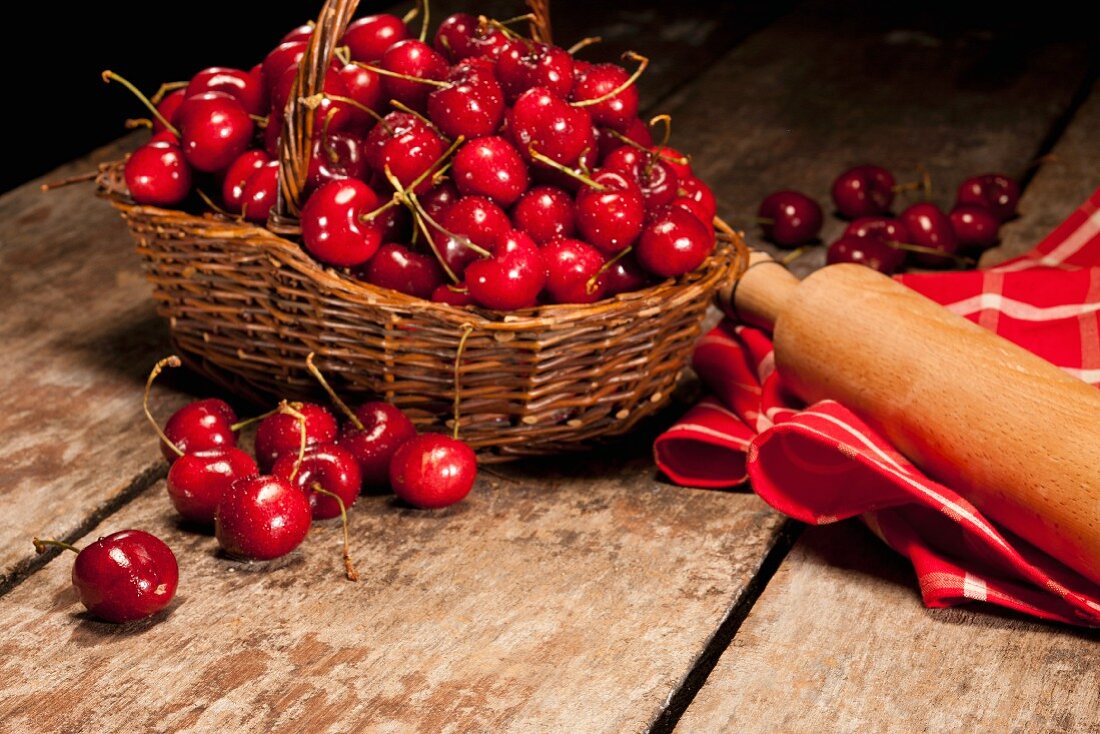 Basket of Fresh Cherries; Rolling Pin and Dish Cloth; On Wooden Table