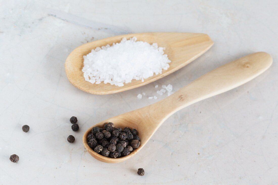 Salt and black peppercorns on wooden spoons