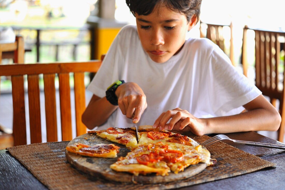 Junge schneidet Pizza in Portionen