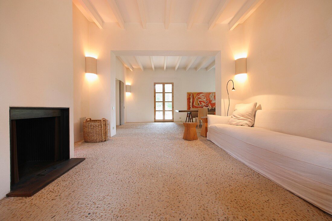 Steinboden mit kleinen Kieselsteinen im minimalistischen Wohnraum mit schlichtem Sofa vor offenem Kamin