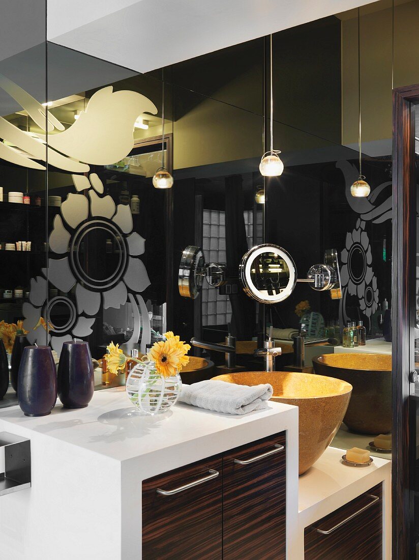 Dark, reflective glass surfaces with floral pattern behind washstand with wooden doors and yellow basin