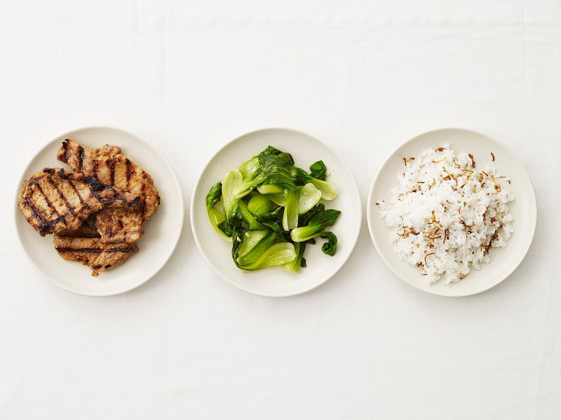 Gegrilltes Schweinefleisch, Pak Choi & Reis auf drei Tellern (Aufsicht)