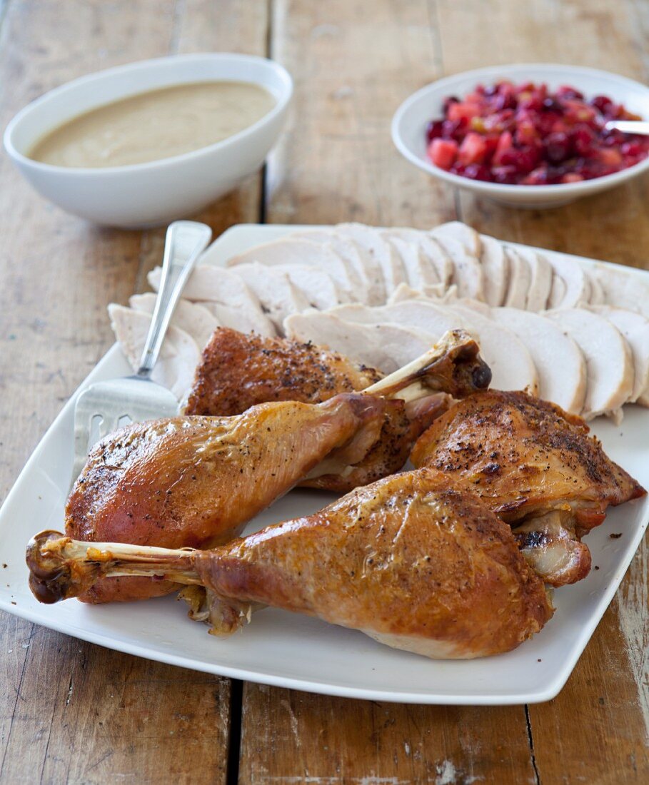 Sliced Turkey on a Platter with Drumsticks; Gravy and Cranberry Sauce