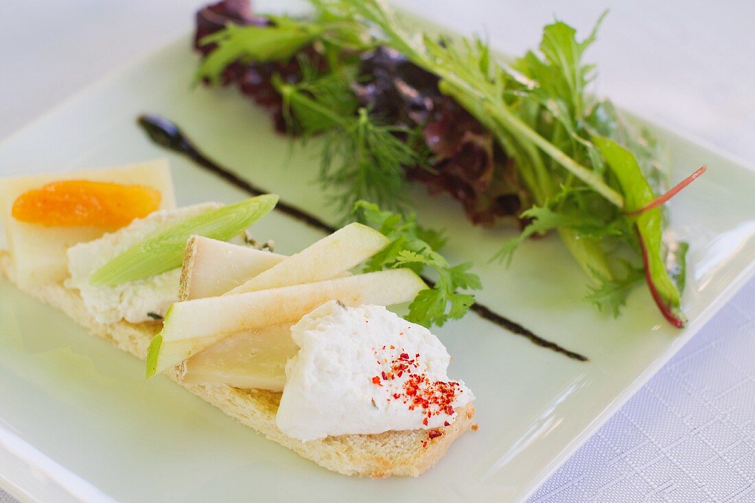 A slice of bread topped with cheese and a mixed leaf salad