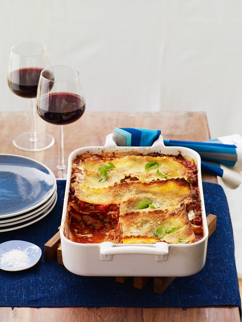 Meat Lasagna in a Baking Dish with Slice Removed; Glasses of Red Wine