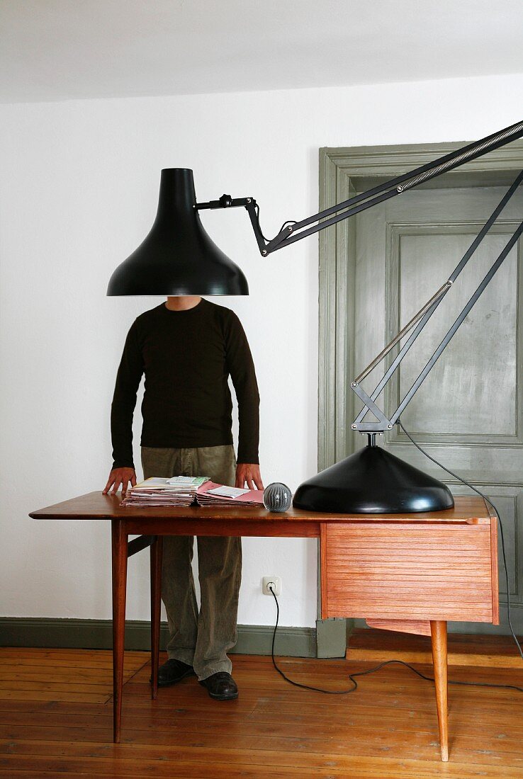 Giant, black retro desk lamp on fifties-style desk with man in background