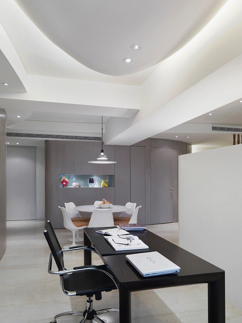 Swivel office chair next to a black office desk in an open living room with a modern recessed ceiling and spotlights