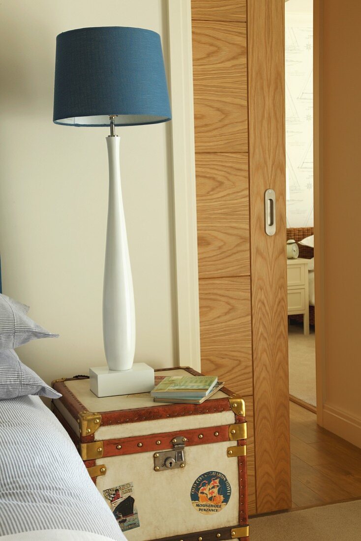 Maritime, blue and white bedside lamp on small steamer trunk; half-open sliding door in background of sleeping area