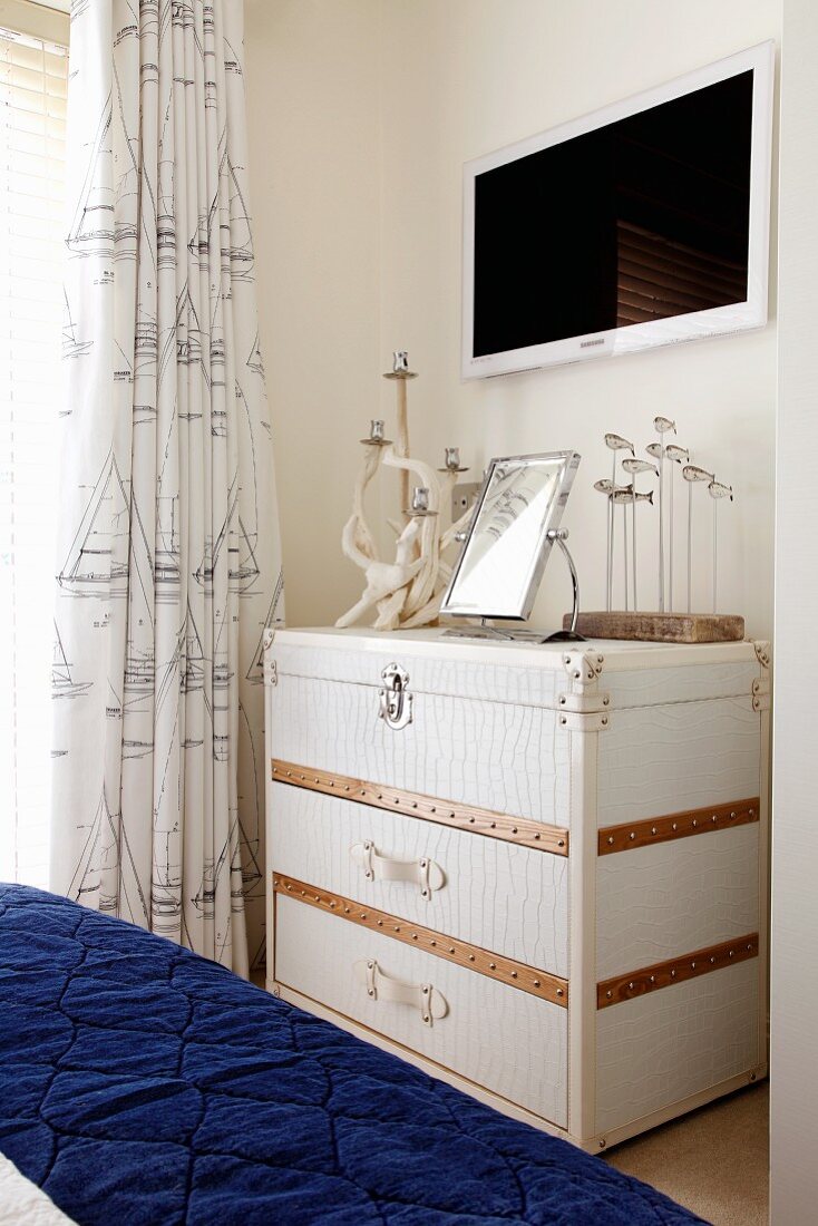White steamer trunk as maritime chest of drawers in bedroom with blue, quilted bedspread in foreground
