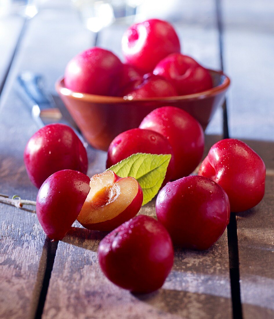 Red plums in and in front of a bowl