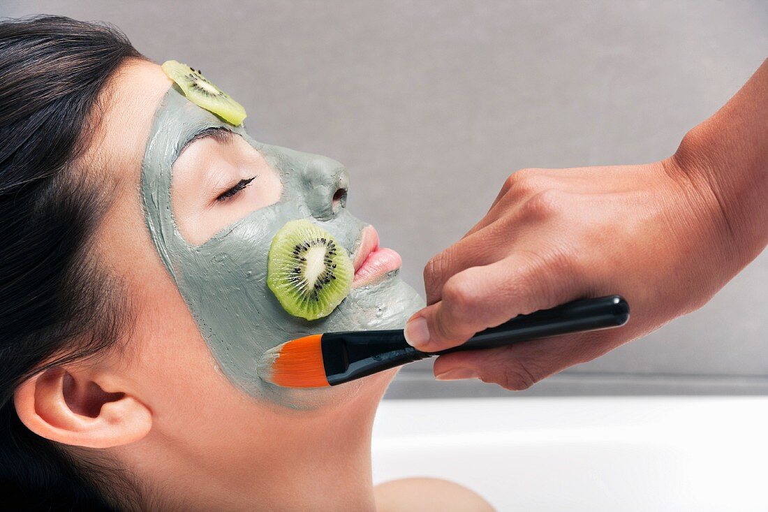 Junger Frau wird eine Gesichtsmaske mit Kiwi aufgetragen