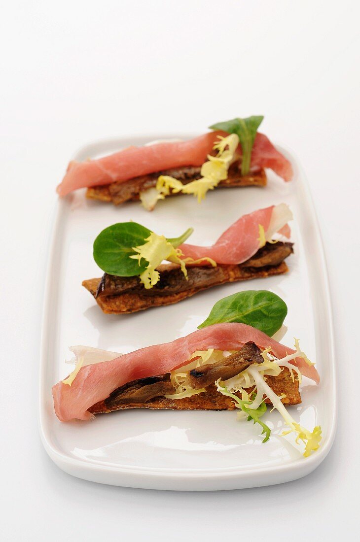 Crackers topped with raw ham and marinated aubergines