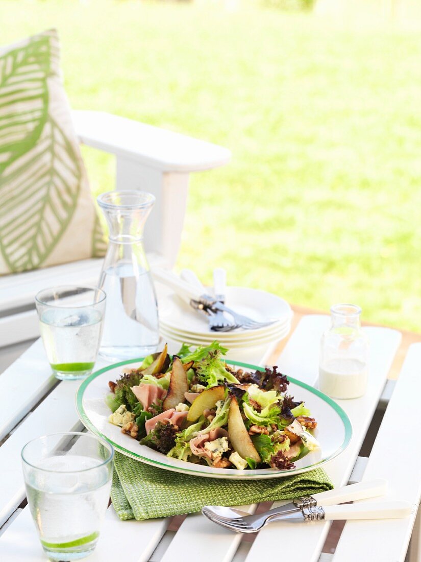 Blattsalat mit Schinken, Birnen und Walnüssen auf Gartentisch