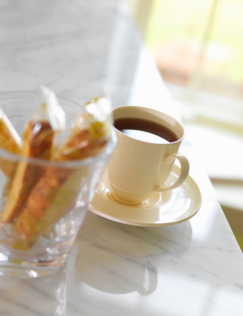 Eine Tasse Kaffee neben Glas mit verpackten Biscotti