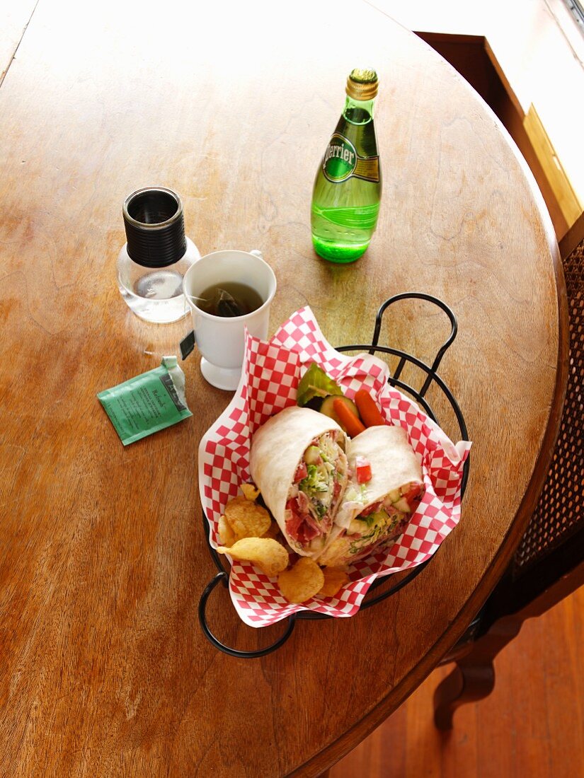Schinken-Käse-Wrap mit Chips auf Tisch mit Tee & Mineralwasser