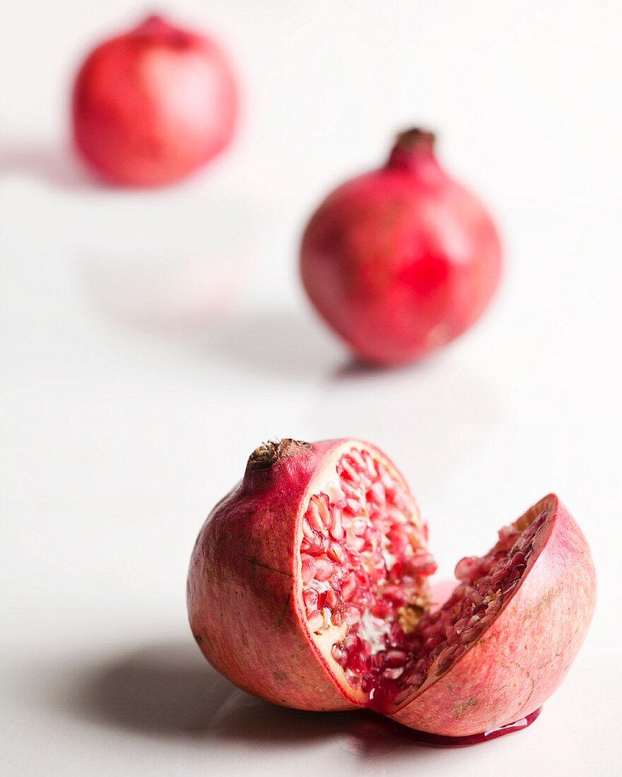 A Pomegranate Cut in Half; Whole Pomegranates in the Background