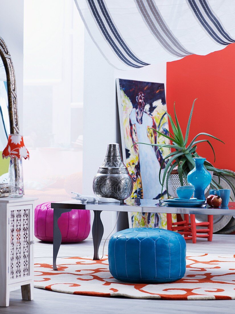 Decorative metal and blue glass vessels on low table and brightly coloured, Moroccan pouffes