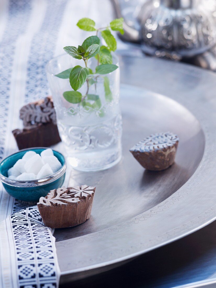 Pfefferminze in Wasserglas, Zuckerschälchen und Muster-Stempel auf Metallschale