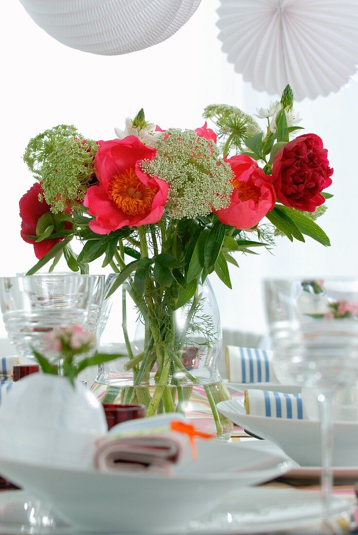 Sommerstrauss in Vase und weiße Gedecke mit Weingläsern auf Tisch