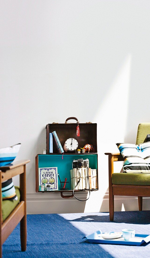 Open suitcases upcycled as shelves mounted on wall between fifties-style upholstered armchairs