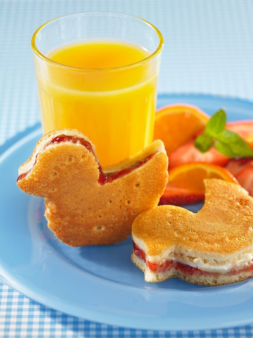 Duck-shaped pancakes filled with strawberry jam with a glass of orange and fresh fruit