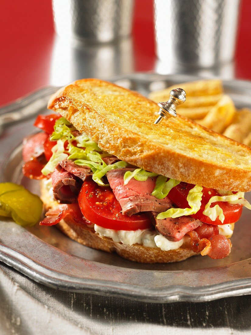 A steak sandwich with tomatoes and bacon
