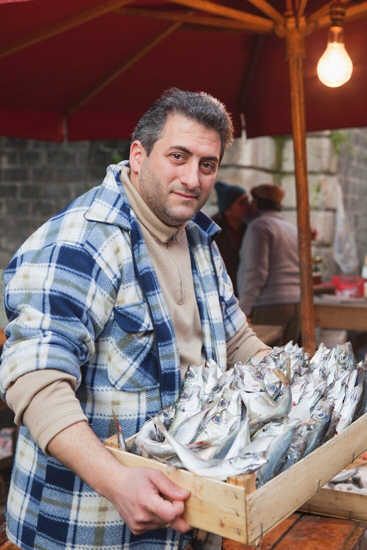 Fischer präsentiert Holzkiste mit frischen Fischen