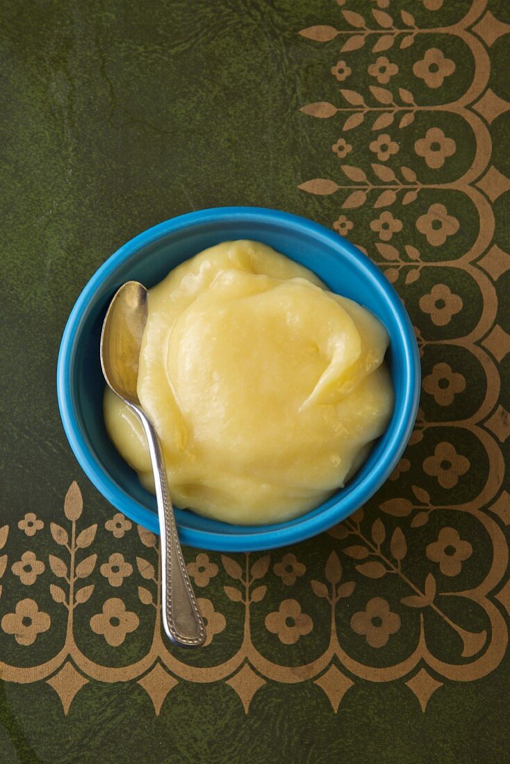 Lemon Curd mit Löffel in einer blauen Schale (Draufsicht)