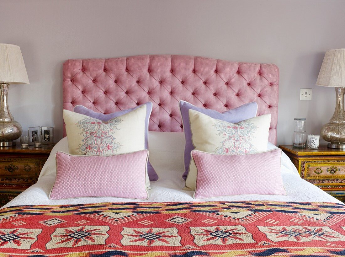 Double bed with scatter cushions against headboard with pink upholstery