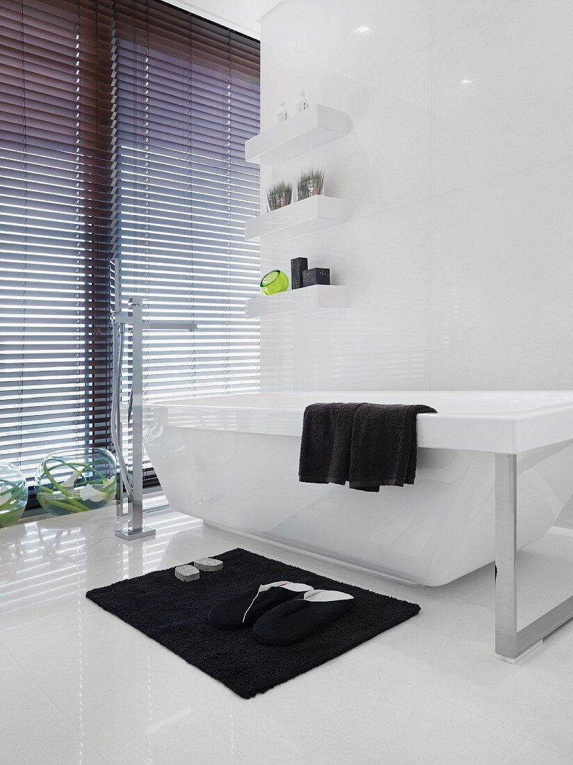 House slippers on a bath mat in front of a free standing designer bathtub with standing bathtub fixtures