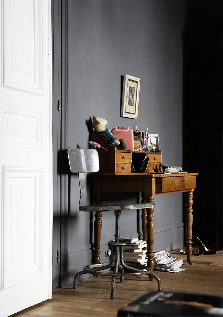 Antique writing desk in front of a dark gray wall next to a white door