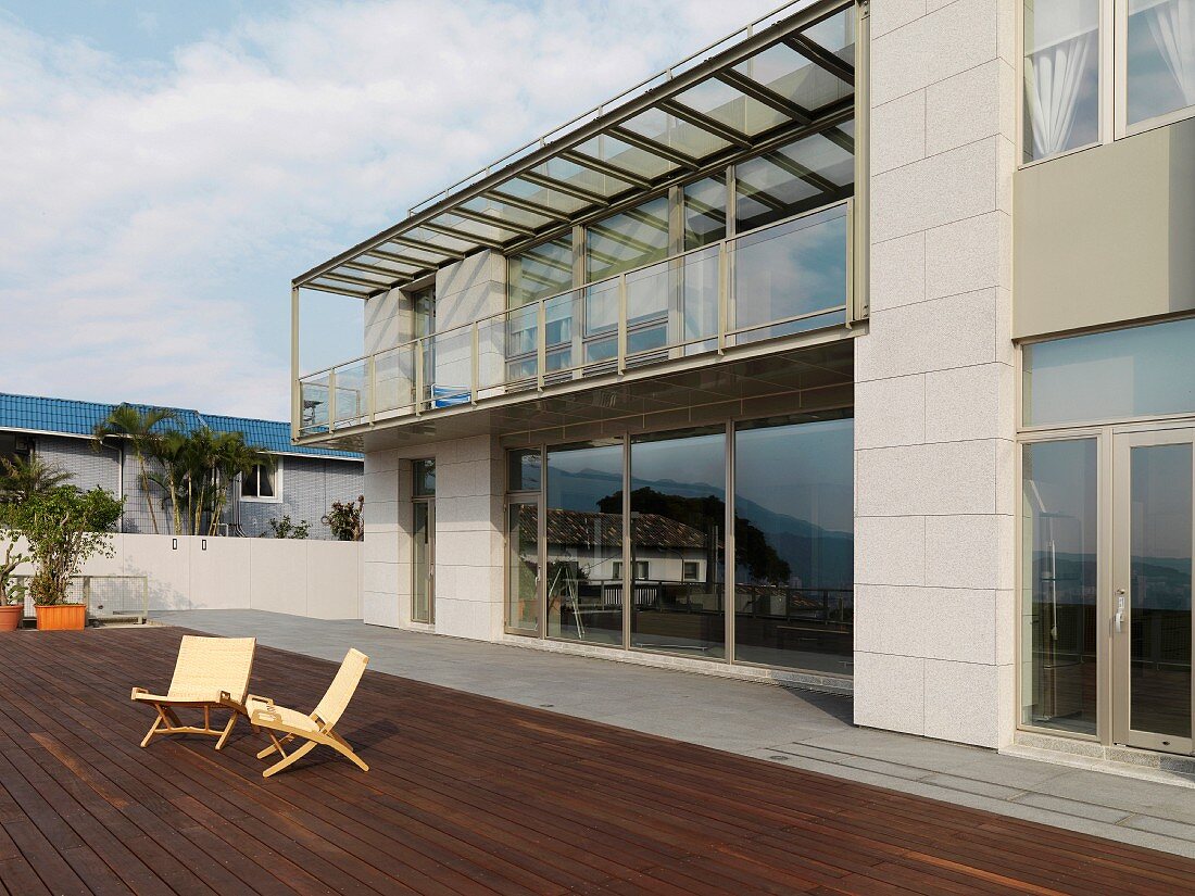 Zwei Klappstühle auf der weitläufigen Terrasse eines modernen Wohnhauses mit Panoramafenstern