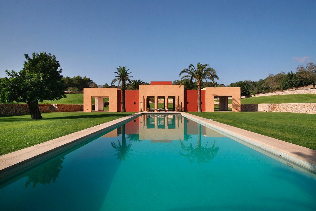 Ein langer Pool mit mediterranem Poolhaus in einer gepflegten Gartenanlage