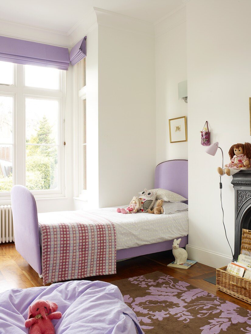 Lilac beanbag on patterned rug and sleigh bed with lilac fabric cover in front of bay window in child's bedroom