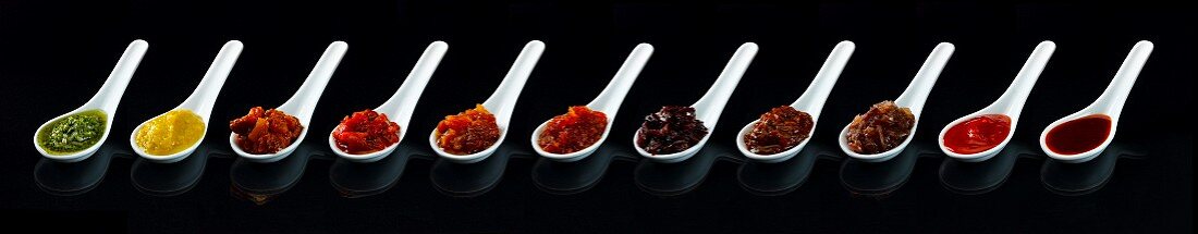 Various different spicy sauces on spoons