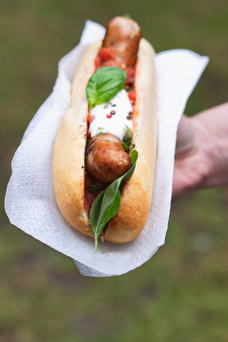 A hand holding a hot dog with tomato salsa and basil