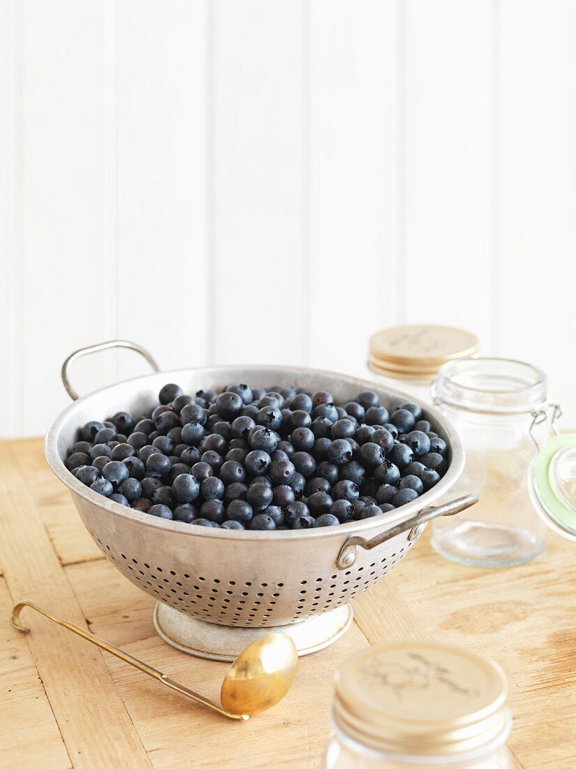 A colander of blueberries and jam jars