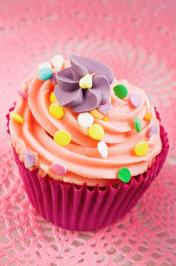 A cupcake decorated with buttercream, sugar sprinkles and a sugar flower