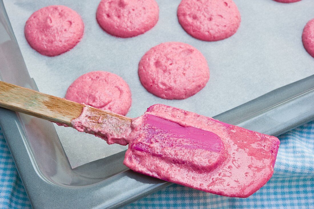 Pinkfarbene Teighäufchen für Macarons auf Pergamentpapier